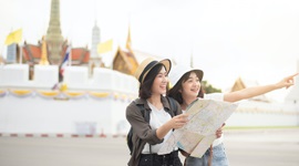 A photo of two Asian women holding a map while one points out into the distance